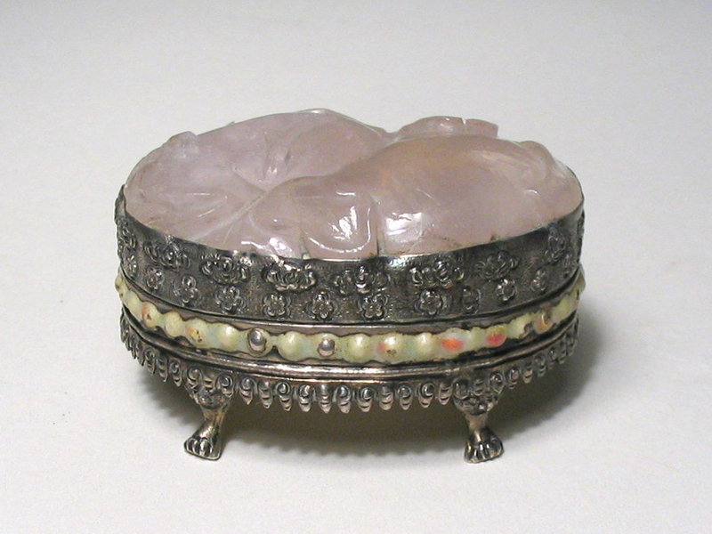 DESCRIPTION:  A pretty little repossee’ silver Chinese export box on short paw-feet legs with a large pink quartz carving inset into the top, carved in the form of a peach and a pomegranate.  The inside has been gold washed and the base bears a stamp “Made in China, Silver.”  The perfect size for holding a favorite ring or earrings, the box is in good condition with wear to the white overlay on the horizontal band; first quarter of the 20th C.  DIMENSIONS:  2” long (5 cm) x 1 ¼” high (3.2 cm).<div id='rater_target1119533'></div>
