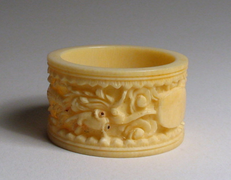 DESCRIPTION:  A Chinese carved ivory napkin ring, the outer band carved with a design of a dragon with inlaid eyes curled about the circumference of the band.  A blank oval plaque awaits a monogram.  Very good condition, and dating from the first half of the 20th C. DIMENSIONS:  1 5/8” outer diameter (4.2 cm) x 1” wide (2.5 cm).<div id='rater_target1129332'></div>
