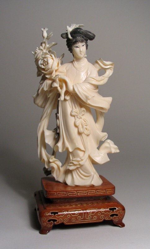 DESCRIPTION:  A finely carved and flamboyant Chinese ivory carving of a woman in flowing robes holding a large bouquet of flowers.  The motion expressed in this carving is excellent, as if a strong breeze is blowing her garments & sashes in the wind.  In her finely coiffed hair she wears a bird ornament.  Dating from the first half of the 20th C. (1900 – 1950), this remarkable carving is in excellent condition; we can find no breaks, chips or repairs anywhere.  Mounted on stand with inlaid silver wire.  DIMENSIONS: Ivory carving is 7.5” high (19 cm); including stand is 9” high (23 cm); 4 3/8” wide (11 cm).<div id='rater_target1129334'></div>
