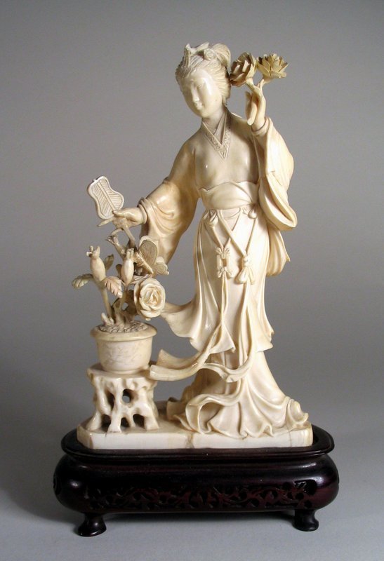 DESCRIPTION:  A beautiful Chinese maiden carved in ivory with flowing robes, standing next to a flower bowl on a stand with a fan in one hand and two roses in the other.  Her face is delicately carved and her hair is pulled back and topped with a bird ornament.  A fine carving in good condition from the early 20th C.  DIMENSIONS:   6 ¾” high without stand (17.2 cm); with stand is 8” high (24 cm).  Stand is 4 ¾” wide (12 cm). <div id='rater_target1139296'></div>
