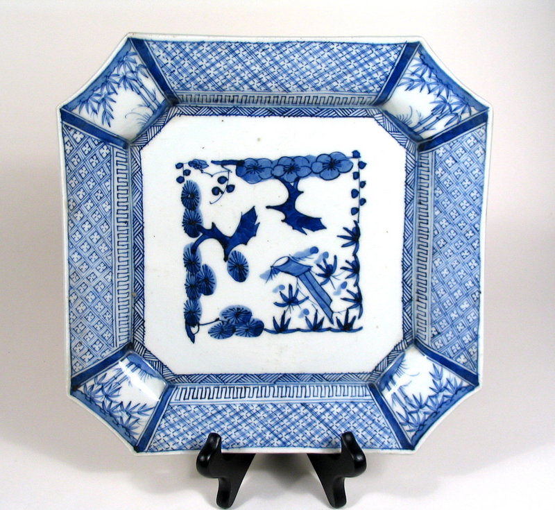 DESCRIPTION: A square porcelain dish by Arita, hand painted in the blue and white “Three Friends of Winter” motif.  The “Three Friends of Winter” was a popular Japanese theme where pine, prunus and bamboo are grouped, said to represent perseverance, longevity and vitality, despite adversity. The raised and flared edges have repeating geometric patterns and bamboo plants are found in each corner.  The plate rests on a round raised foot with blue designs on the undersides.  Produced in the early 1900’s, this plate is in very good condition with no chips or repairs.  DIMENSIONS: 10 ½” square (26.7 cm) x 1 ¾” high (4.5 cm). <div id='rater_target1171560'></div>
