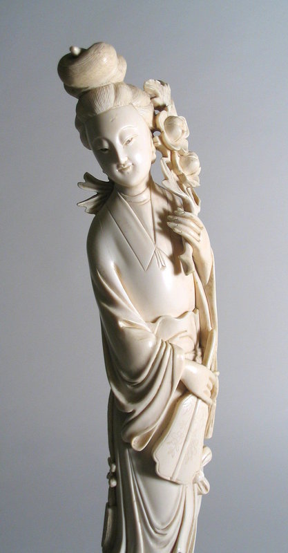 DESCRIPTION:  A tall, antique Chinese ivory carving of a beautiful maiden dressed in flowing robes holding a bouquet of flowers her raised left hand and a fan in her right. Her serene face is accented by coiffed hair tied up in a knot. Very good condition, no repairs.  DIMENSIONS: 14” tall without stand (35.5 cm); 15 ¾” tall with stand (40 cm). <div id='rater_target1181447'></div>
