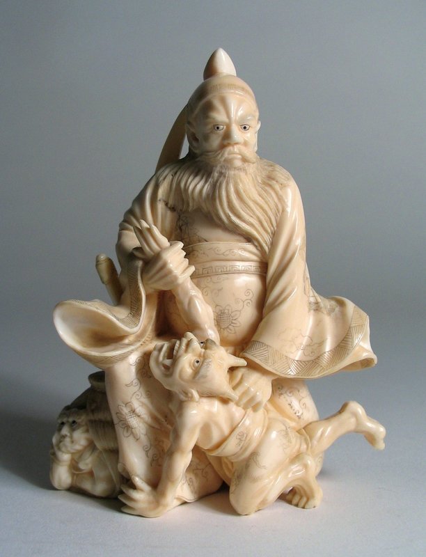 DESCRIPTION: A carved Japanese ivory okimono of the Demon Queller, Shoki, subduing the horned oni crouched at his feet.  The stern, bearded Shoki stands clutching the oni’s arm while the oni is pushed to his knees, crying in terror.  Another small oni is hidden in a nearby sack, oblivious to his potential danger.  Shoki’s sleeves swirl with the action of capturing his foe and his robe, hair and spear are finely detailed in the back view. Meiji Period; very good condition with no chips or repairs.  DIMENSIONS: 4 ½” high (11.5 cm) X 3 ¾” wide (9.5 cm) 
<p>CULTURAL BACKGROUND: Oni are small demons from Japanese folklore. These popular imps are widely featured in Japanese art, literature and theatre, growing out of the religious traditions of Shintoism and Buddhism in Japan. In the Edo Period the demons began to be depicted with humor, more mischievous than dangerous.  In netsuke figures and other carvings, this humor was shown as they played tricks and practical jokes upon their enemy Shoki, the Demon Queller.
<div id='rater_target1183504'></div>
