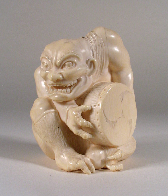 DESCRIPTION:  A fine Japanese ivory carving of a fierce looking, crouched oni with teeth barred in an wicked grin. Oni are creatures from Japanese folklore, variously translated as demons, devils, ogres or trolls. Popular characters in Japanese art, literature and theatre, they grew out of the religious traditions of Shintoism and Buddhism. This one holds a drum between his three-clawed hands while his feet are depicted with two claws each. A fine Tokyo School carving, it dates from the Meji Period (1868 – 1912) and is in very good condition with minor fine hairlines on the head and shoulder region; plaque on the base is unsigned. DIMENSIONS:   3 ¼” high (8.3 cm) x 2 ½” wide (6.4 cm).<div id='rater_target1192450'></div>
