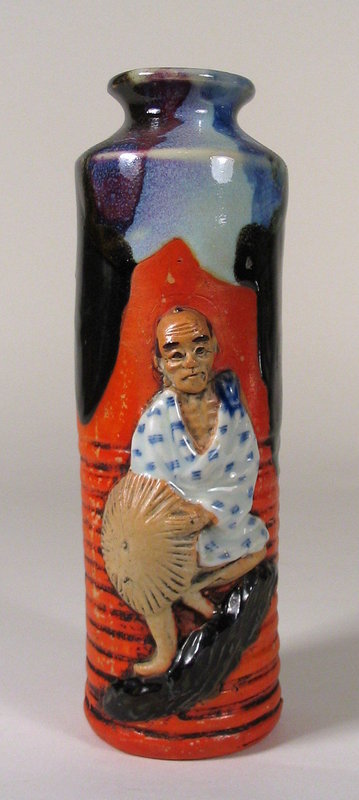 DESCRIPTION:  A Japanese Sumida vase with oval neck rim covered in a rich, thick flambé glaze running midway down the vase.  A high relief figure of a man balanced on a rocky ledge, holding an umbrella, is contrasted against the red, ribbed body of the vase.  Excellent condition with no chips.  For size comparison with our other Sumida listings, numbers CP72 & CP99, see the last photo.  DIMENSIONS:  8" high (20.3 cm) x 3" diameter (7.6 cm).  

<P>ABOUT SUMIDA EARTHENWARE POTTERY: This charming and highly collectable studio pottery originates from the Sumida River area in Japan (near Tokyo).  Produced primarily for export from the late 19th Century through the early 20th Century, this form of pottery is valued for the uniqueness of its handmade relief figures of people and animals engaged in various activities, often humorous or depicting scenes from folklore.  The tops are usually covered with a thick glaze in earth tones while the bodies of the pieces have an applied “cold paint” (usually red).
<div id='rater_target1214307'></div>
