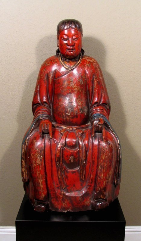 DESCRIPTION:  A large, museum quality, carved and lacquered Chinese sculpture of the Taoism deity Hsuan Tien Shang-ti, dating from the Ming Dynasty, c. 1500's.   The Supreme Emperor of the Dark Heavens, Hsuan Tien Shang-ti is known by numerous titles within China; he is best known to foreigners and laymen as the Northern Emperor, Pei Ti (Cantonese Pak Tai) or Chen Wu.  
<p>Here he is carved in a seated posture, draped in a red lacquered robe with blue trim, his hands resting on his knees with fingers in a traditional Taoism pose.  His waist is tied with a sash and his shoes turn upward.  A large figure such as this would have been crafted for worship in a temple or for the family shrine of a scholar or Chinese official.  The red lacquer on this figure is frequently seen in quality 16th and 17th century carvings.  
<p>HISTORY/PROVENANCE:  This figure was originally the property of a Chinese scholar and was passed down through the generations in a single family. During the Cultural Revolution in the late 1960's, when owning such works was forbidden, this sculpture was painted brown to hide its age.  The former owner/collector from Taipei purchased it in Beijing over 25 years ago and had it professionally cleaned to expose its original red lacquered surface.  CONDITION:  The patina and aged surfaces support the date of 16th C. to 17th C. (1500's - 1600's).  While there are superficial losses or cracks to the red lacquer in places, there is no major damage, deep cracks or loose portions; the non-lacquered wood on the base has some worm holes and minor age related rot.  DIMENSIONS:  33" high without stand (83.8 cm) x 18" wide (45.7 cm).  <div id='rater_target1249154'></div>
