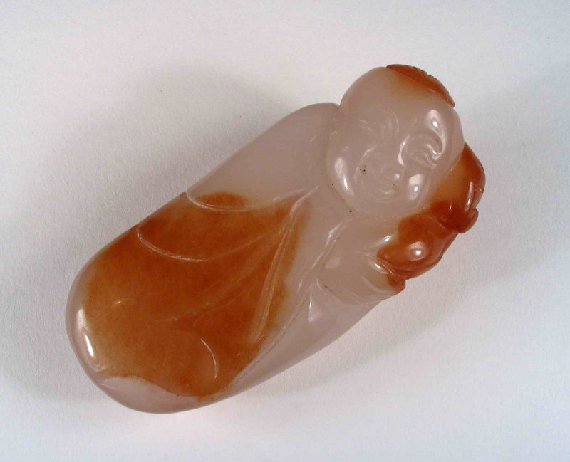 DESCRIPTION: A simply carved agate rubbing stone in the form of a Chinese boy carrying a ruyi. The semi-precious stone is pure white with brown inclusions that have been incorporated into the design as the boy’s cloak, hat and ruyi, which he carries on his shoulder. A small hole has been drilled through the ruyi at the back of the head for stringing and wearing from the belt as a toggle. Stones such as these were meant to held, rubbed and fondled, with this one fitting perfectly into the palm of the hand, the stone feeling cool and silky smooth to the touch. From an estate, we estimate the carving to be from the mid 19th to early 20th century. Excellent condition, no cracks or losses. DIMENSIONS: 3 ¼” long (8.5 cm) x 1 ½” wide (4 cm).  <div id='rater_target1270668'></div>
