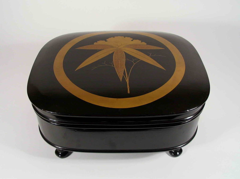 DESCRIPTION:  Dramatic in its bold yet simple design, this Japanese lacquer box makes a striking statement.  The background of this large box is lacquered in a mirror-like, black ro-iro ground, with a vivid gold lacquer design on the lid of bamboo superimposed over a ginko leaf, all within a gold circle.  The box is supported on four curved feet, and the interiors are brilliantly lacquered in orange-red.  This box is in excellent condition, with very minor “bumps” to the outer lid, and the red interior appearing almost new.  Dating from approximately 1900 to 1920, this would make a spectacular table-top piece for any Asian or modern interior.  DIMENSIONS:  14 ½” wide (35.5 cm) x 11 ¾” deep (30 cm) x 6 ¾” high (17.2 cm).  <div id='rater_target1284101'></div>
