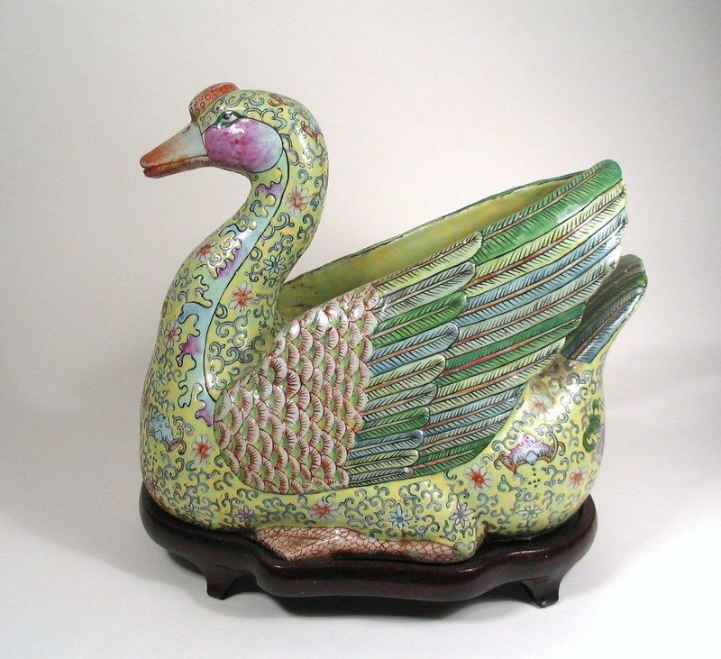 DESCRIPTION:  This large and impressive Chinese porcelain goose, painted in a famille rose pallet, is seated on folded legs with upturned tail and rests on a raised, fitted wood stand.  Modeled with a slightly turned head and erect wings that touch at the tips, the body is enameled in a yellow ground with a pink bat and green scrolling vine motif, the lightly molded and naturalistically marked feathers in shades of blue and green.  Unmarked base but judged to be late Qianlong to Jiaqing Periods (CIRCA 1780 - 1820).  This remarkable goose is molded as one piece (not a tureen) and its most likely use was as a striking table centerpiece.  CONDITION:  Very good, no chips, cracks or repairs; some rubbing and age related discoloration to enamels in spots.  DIMENSIONS:  14" long (35.5 cm) x 9 1/2" wide (24.2 cm) x 12" high (30.5 cm).  Stand is 2" high (5 cm).  Weight: a hefty 14.5 lbs. (6.577 kg) including stand. <div id='rater_target1289902'></div>

