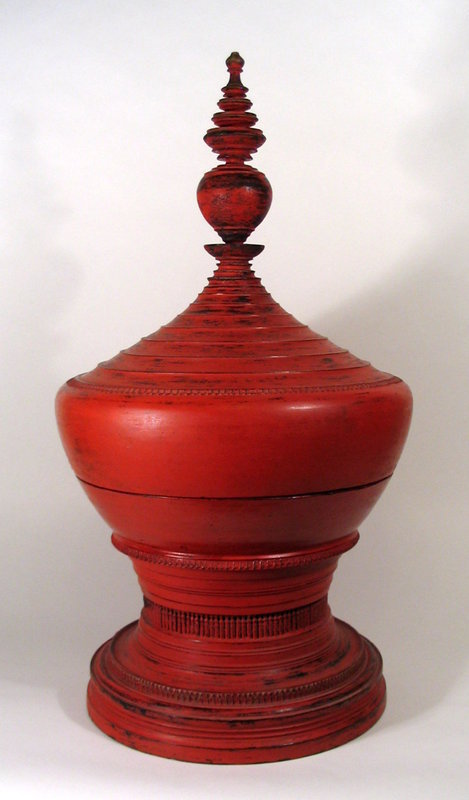 DESCRIPTION:  From our Southeast Asia Collection, a large and classic 19th century Burmese Hsun-ok constructed of wood that was first lacquered in black, and then covered in successive layers of cinnabar colored lacquer called hinthabada.  Over time, through use and handling, the cinnabar lacquer has worn off in some areas to reveal the black lacquer base coat underneath, resulting in an attractive negoro effect.  This particular vessel has graceful, stepped shoulders, a tall spire with large center bulb and is raised on a wide base with carved vertical balusters.  
<p> These classic offering vessels were used for carrying food to the monastery and are elegant examples of traditional Burmese lacquer and woodworking, reflecting Burmese society's devotion to the monastic life.  Today they make dramatic decorating and accent pieces in the West.  PROVENANCE:  From the estate of art collector, Dr. Edward Gerber. CONDITION AND DIMENSIONS:  Old nicks and repairs as are common to these antique vessels.  31 1/2" high (80 cm) x 17" diameter (43 cm).  
<div id='rater_target1292244'></div>
