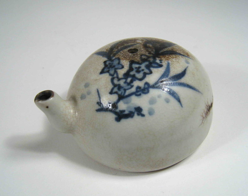 DESCRIPTION:  One of the necessary calligraphy tools on the Chinese scholar’s table was a small container to hold water and drip it onto the inkstone for the purpose of mixing the ground ink. These small but important objects were crafted so that one measured drop at a time could be poured to ensure the proper ratio of ink to water while mixing.  This bulbous blue and white ceramic dripper would have been submerged in water to fill, and then held between the thumb and forefinger with the thumb covering the small hole at the top to control the rate of drip from the spout.  The dripper is covered with a white glaze that has crackled and filled in areas with a darker color (perhaps ink), and is hand decorated with a spray of blue flowers.  Excellent condition and dating from the Qing Dynasty, 19th C.   DIMENSIONS:  3” wide (7.6 cm) x 1 3/4” high (4.5 cm).  <div id='rater_target1292836'></div>
