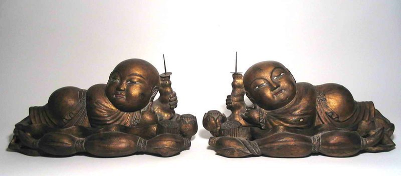 For the pair<br /><br />
DESCRIPTION:  A pair of decorative, large and captivating carved wooden figures of two reclining “lotus boys,” each with a candle stand in one hand. The fat-cheeked, gilded babies are carved separately from their large lotus leaf bases, which are complete with curled edges and seed pods.  In Chinese folklore, such figures represent the wish for many sons - “as many as the seeds in the lotus pod.”  These large figures are absolutely charming, and would make wonderful focal points on a Chinese altar table or dining buffet.  Dating from the Republic Period (1911-1949), they are both in very good condition. DIMENSIONS: Each figure is approximately 18 ½” long (47 cm) x 9” wide (22.8 cm) x 9” high (22.8 cm) to the top of the candle prick.  <div id='rater_target1299974'></div>
