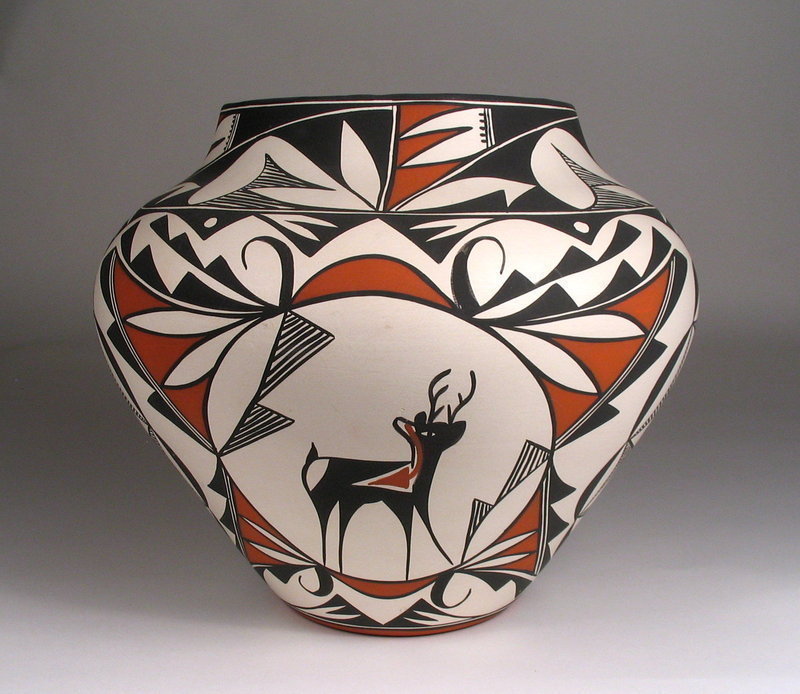 DESCRIPTION:  A striking Acoma pottery olla with dramatic traditional graphics in white, black and orange.  This greenware olla is skillfully painted in traditional designs including hatched (symbolizing rain), stepped (representing clouds) and curvilinear, with distinctive "heartline" deer figures and bold flowers.  These designs speak of water, fertility, the life cycle, the earth and sky, and their interrelationships to each other.  The concave bottom is signed, "Acoma Pueblo, New Mexico, Louise Amos." C. 1980 and in very good condition with no chips.  Please see the last photo for a size comparison with our other Acoma pottery pieces in our Santa Fe gallery; this olla is centered in the front middle.  DIMENSIONS:  8 1/2" high (21.6 cm) x 9 3/4" diameter (24.7 cm). 
<p>ABOUT ACOMA POTTERY:  Thin, hand fired walls (a common and sought after characteristic of Acoma pottery), light weight, and geometric designs characterize Acoma pottery.  The Acoma Pueblo, also known as "Sky City," is located 50 miles west of Albuquerque near Enchanted Mesa, and is one of the oldest continually inhabited sites in North America. The area is home to particularly good clay, which potters mix with a temper of crushed potsherds. This results in the ability to produce very thin and lightweight, yet strong pottery. Traditional designs range from complex geometrics to abstract animal, floral and figurative forms. Coloration consists predominantly of black and white, or black, white and orange although other colors also appear infrequently. Acoma clay is grey in color and potters achieve their white surface with a slip of kaolin, a naturally occurring chalky material that is a brilliant white. Black can be made from crushed iron-rich hematite and/or the liquid from boiled wild spinach, which are often mixed together.  
 
<div id='rater_target1300091'></div>
