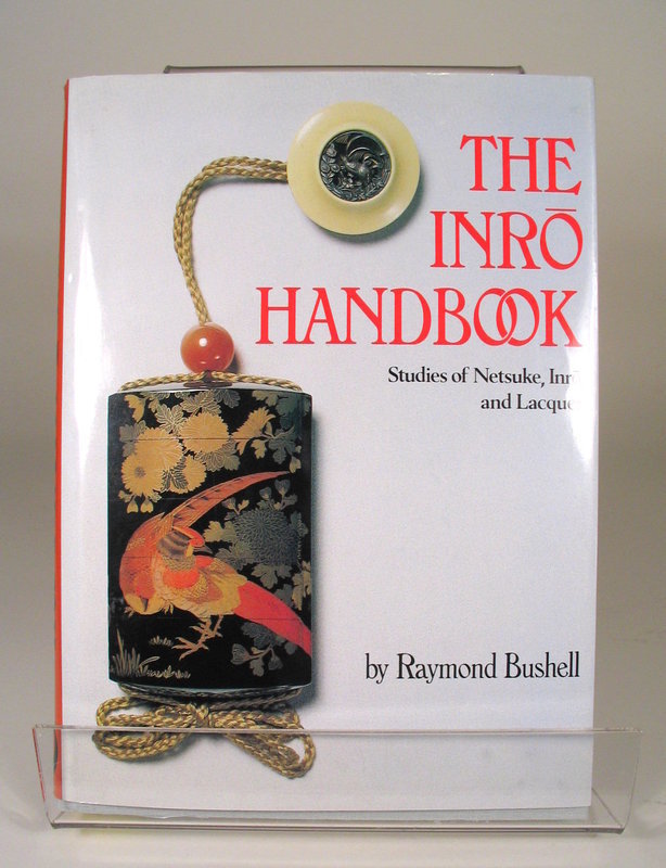 DESCRIPTION: “The Inro Handbook, Studies of Netsuke, Inro and Lacquer” was written for collectors who have discovered the delights of the miniature Japanese art forms.  This authoritative and enlightening book offers a wealth of valuable information and is written by one of the foremost collectors and scholars in the field, Raymond Bushell. Affording entry into a world of fascinating design and superb craftsmanship, the book covers the subject in a thorough manner with beautiful color illustrations of 108 distinguished inro and their accompanying netsuke. Included are highly informative essays on the making of inro including materials and techniques.  It also furnishes an extensive list of lacquer artists’ signatures with 386 photos. Hardcover; in pristine, like new condition with perfect dust jacket and interior; Published by Weatherhill, Inc., New York; first edition, third printing. DIMENSIONS:  10 ½” (26.6 cm) x 7 ¾” (19.6 cm).<div id='rater_target1305474'></div>
