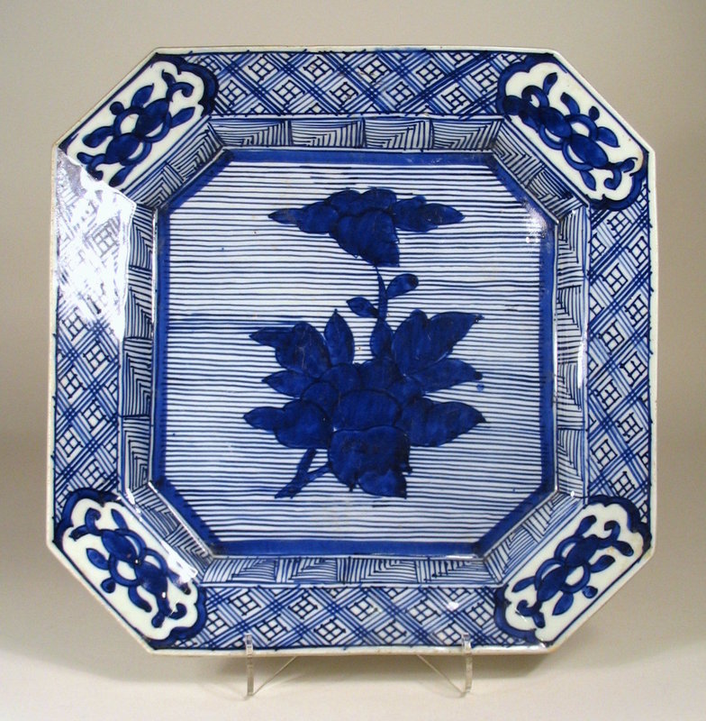 DESCRIPTION: This large, boldly decorated early 19th century Japanese Arita sometsuke (blue and white) porcelain dish in square form (“kaku-zara”) is hand painted in deep cobalt blue with a center floral design against thin parallel lines. This center ground is bordered by diaper designs around the raised rim with floral cartouches at each corner.  Such a dish was used in Japanese tea ceremonies for serving raw fish or shellfish. The reverse is hand painted with stylized decorations in cobalt blue surrounding the high unglazed foot rim.  DIMENSIONS: 11 ½” square (29 cm) x 2” high (5 cm).  <div id='rater_target1310923'></div>
