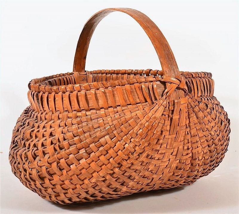 DESCRIPTION:  A very good woven oak-splint basket in lobed buttocks form, used as a field gathering basket or a market basket for goods. This large early 1900’s Pennsylvania basket has a sturdy bentwood handle with double bentwood-wrapped rims; old varnish finish. Very good condition with minor usage wear.  For size reference, the last photo in this listing shows this basket displayed on top of our Country Corner Cabinet (#A-CBL2).  DIMENSIONS: 20” wide x 17" high.  
<div id='rater_target1365182'></div>
