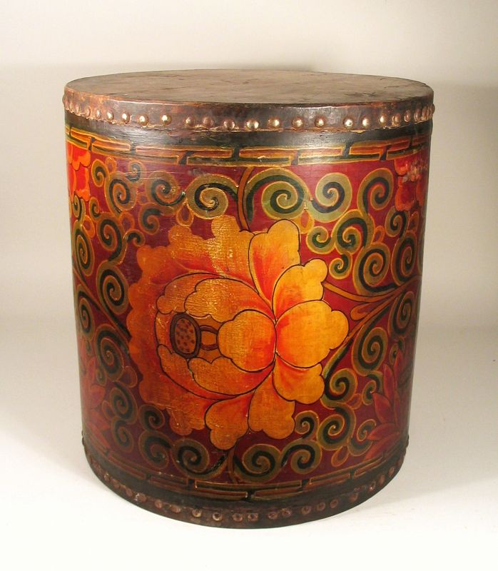 DESCRIPTION:  An antique hand-painted ceremonial drum with vivid motifs of large flowers with curling green tendrils against a red ground. Both ends of the drum are covered in animal hide and secured with round-headed metal studs. This highly decorative drum makes a perfect little end table, or adds a touch of exotic to any décor. Very good condition with minor rubbing in spots. DIMENSIONS: 16 5/8” high (42.2 cm) x 15 5/8” diameter (39.6 cm).   
<div id='rater_target1368993'></div>
