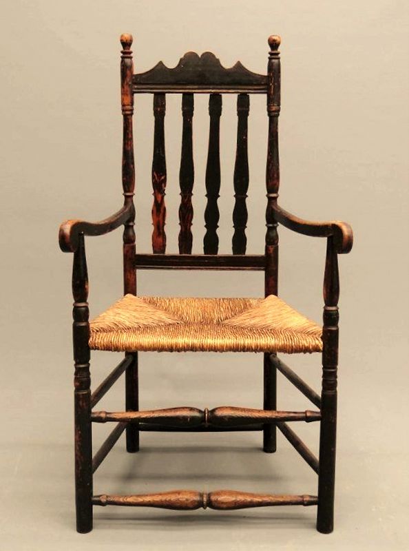 DESCRIPTION: An 18th c. banister back armchair having a scalloped crest rail, turned finials, straight bottom rail, bulbous front spindles, and rush seat.  Good condition with age appropriate wear, original black paint.  See our listing #A-CH2 for a near match companion chair to make a pair. DIMENSIONS:  23” wide x 19.5” deep x 44.5" high; 18" seat height.
<div id='rater_target1372050'></div>
