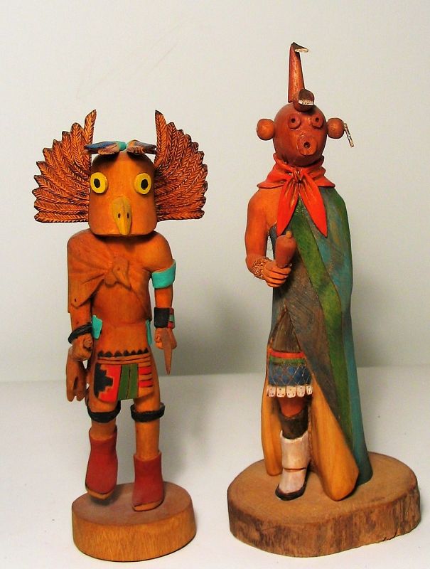 DESCRIPTION: A hand carved and painted pair of Native American Hopi Kachina (or Katsina) dolls, one in a long green and blue robe with red neck kerchief, the other in an elaborate headdress.  Each is signed, one signed “Mongwa, D. Scott, Old Oraibi” and the other “D. Harvey, Koyemsi, Hopi Tewa, ‘96”. DIMENSIONS: Tallest 10.75” high. 
<p>CULTURAL BACKGROUND: The Hopi people live primarily on three mesas in northeastern Arizona, about 70 miles from Flagstaff. Hopi katsina figures, also known as kachina dolls, are figures carved typically from cottonwood root by Hopi people to instruct girls and new brides about katsinas or katsinam, the immortal beings that bring rain, control aspects of the natural world and society, and act as messengers between humans and the spirit world. The katsinas are known to be the spirits of deities, natural elements or animals, or the deceased ancestors of the Hopi. Katsina figures originated in the late 19th century and continue to be carved to this day adhering to Hopi tradition.   
<div id='rater_target1392152'></div>
