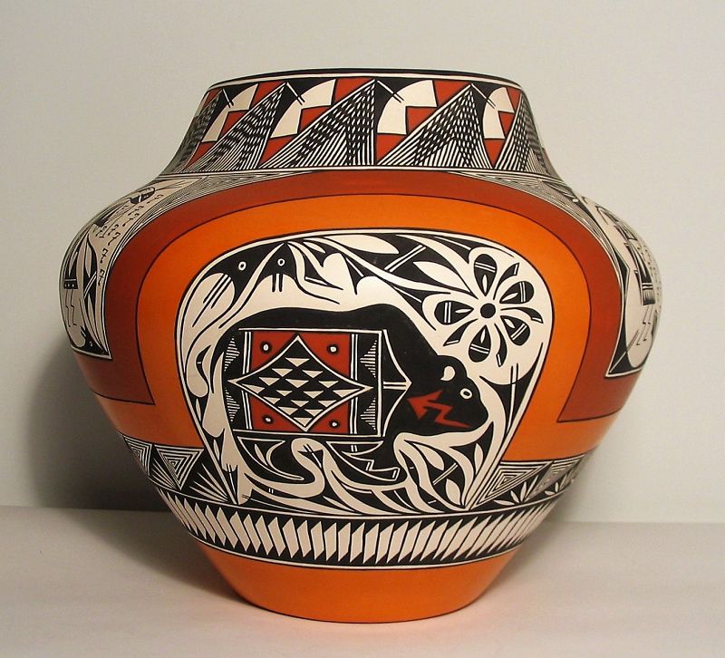 DESCRIPTION: A fantastic Acoma pottery water jar of large size with a wonderfully complex polychrome design containing bear and Kokopelli figures. A double rainbow of light and dark sienna bands divides this beautiful greenware olla into six cartouche segments, three larger ones with bears below the arched rainbows, each with different background designs, and three smaller ones with stylized Kokopelli figures (fertility deities) playing flutes.  Additional geometric designs in black on white are executed with clean, crisp lines.  A large statuesque piece with broad shoulders, it is signed "Acoma, N.M. "Sky City" R.T.P." Late 1900s, very good condition. DIMENSIONS: 12-1/4" x 13-1/2"
<p> Acoma Pueblo, NM, is the oldest continually inhabited community in the United States and consists of several villages, the best known being “Sky City.” It sits atop a 357-foot mesa that was inaccessible to enemy raids for centuries because there was only one way up, and that was a heavily guarded narrow stairway where one had to use handholds to ascend (an effective defense). Today there is a paved road to the top, however the pueblo remains in its original state with no running water, electricity, or telephone lines. A little more than 50 people live up on top of the mesa year round, with the remainder living in the farming villages below.  Acoma Pueblo artists are known for their intricate fine black-line pots which are highly sought by collectors.  Interestingly, every Acoma pot has an old pot incorporated in it. The potters take old pot shards and grind them up to use as temper for a new pot. 
<div id='rater_target1397434'></div>
