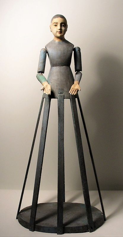 DESCRIPTION: A stately santos cage doll (a Virgin Mary bastidor) with blue bodice and hand carved head with glass eyes, the face with a beautiful, peaceful expression.  Her arms are articulated at the shoulder and elbow, and eight wooden slats form the frame. A lovely santos, good condition, minor paint chips. DIMENSIONS: 29'' high x 12.5'' wide at the base. 
<div id='rater_target1398319'></div>
