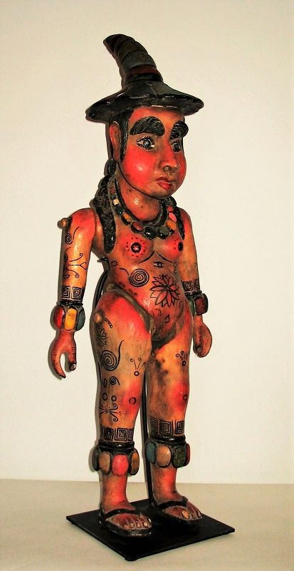 DESCRIPTION:  A Mexican carved wood sculpture of an indigenous female, used as a processional “pole puppet” during Mexican festivals.  The polychrome decorated figure has articulated arms and legs and a hole running through the waist through which a pole or dowel would be inserted.  The pole, when mounted with several puppets, would be used in festival processions, with the bouncing of the pole animating the movements of the figures. This nude figure with bushy eyebrows and hair is covered in tattoo like designs, wears a pointy hat, and sports large neck, wrist and ankle beads.  A custom stand made specifically for this figure is included.  CONDITION: Mild scuffing to paint, good sturdy condition. DIMENSIONS:  33” high with stand x 12” wide x 7"deep.
<div id='rater_target1399437'></div>
