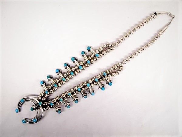 DESCRIPTION: Beautiful Navajo sterling silver Bisbee blue turquoise squash blossom necklace by Navajo artist, Phil Garcia. There are fifteen silver squash blossoms, each with light blue turquoise stones on each end.  A classic Phil Garcia design, necklace is easy to wear as it is less “clunky” than the larger sized squash blossom necklaces often seen.  Hook clasp.  DIMENSIONS:  Measures 14'' end to end; blossoms measure 1'' in length; naja measures 1.5'' x 2''; stamped sterling and hallmarked PG; 60.68g in total wt.<div id='rater_target1473793'></div>
