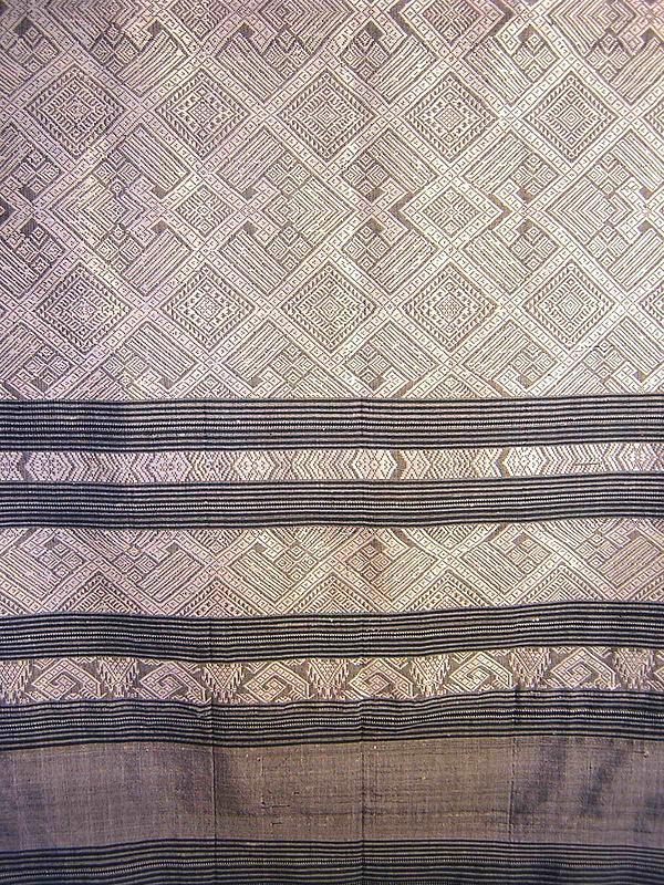 DESCRIPTION:  An exquisite blue/grey & white textile hand woven with raw silk.  This textile originates from Laos and was worn as part of the traditional costume of Laotian women.  The design is executed in diagonal white silk squares with geometric designs, intersected with horizontal blue/grey stripes of varying widths on each end, and finished with a knotted silk fringe.  This textile would have originally been worn as a skirt wrap, and would be gorgeous and fashionable serving that same function today.  It would also make a beautiful wall hanging, or can be used as a shawl gathered around the shoulders.    This Pha Baeng is 30 to 40 years old and is in excellent condition.  DIMENSIONS:  Larger than most at 34” wide x 70” long.<div id='rater_target331058'></div>
