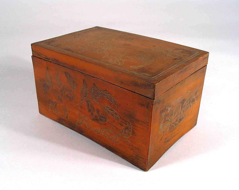 - On Hold<br /><br />
DESCRIPTION:  A small, rare box crafted in the tiehuang technique, marked and dating from the Qianlong Period (1736 -1795).  The outer surfaces of the box are all carved with naturalistic motifs, the top featuring a bird resting on a blooming peony branch (signifying nobility and wealth).  The two wider sides also feature carved peony branches, while the two ends are carved in a lily motif.  The inner lid carving is raised and holds an interesting, hidden surprise.  Here a man and woman have disrobed and the man is making amorous advances toward the female.  This scene is set inside an interior room (perhaps a scholar's studio) furnished with tables, benches, and a cabinet full of stacked manuscripts.  The footed base of the box is slightly concave on all four sides.  A carved Qianlong mark is on the bottom, and the box is of the period.  CONDITION:  Ink stains on the box, a few minor age cracks.  DIMENSIONS:  4 ¾” long x 3 ¼” wide x 2 ¾” high.  
<p>TECHNIQUE: The tiehuang (“applied yellow”) technique was first used in the 18th century, and is not commonly known outside of China.  In this technique, thin layers of the pale golden inner skin of a section of bamboo stem is removed, in strips or sheets, flattened under pressure, and applied as an appliqué on another wood or bamboo item.  This could then be carved, and enabled the bamboo carvers to break free from the circular shapes dictated by the medium. <div id='rater_target465865'></div>
