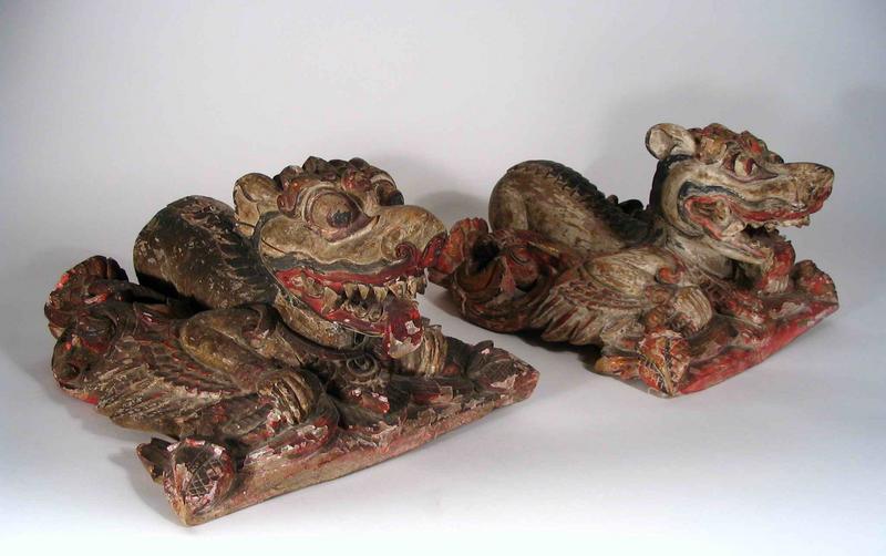 Pair<br /><br />
DESCRIPTION: A fantastic pair of antique carved and polychrome wood figures, originating from Bali and dating from about 1900 to 1920.  These winged wolf-like creatures, crouching within a bed of flowering vines, are quite alert with their mouths open and teeth barred.  Some of the original pigments of gilt, red, white and black remain.  Indonesia is noted for its fanciful wood carvings that appear on temples and within shrines.  These fantastic creatures are a testament to the imagination and skill of these carvers. This pair has been recently released from a private Asian collection where they have been held for many years.  DIMENSIONS:  Each approximately 11 ½” long (29 cm) x 10 ¼” wide (26 cm) x 7” high (18 cm).<div id='rater_target574682'></div>

