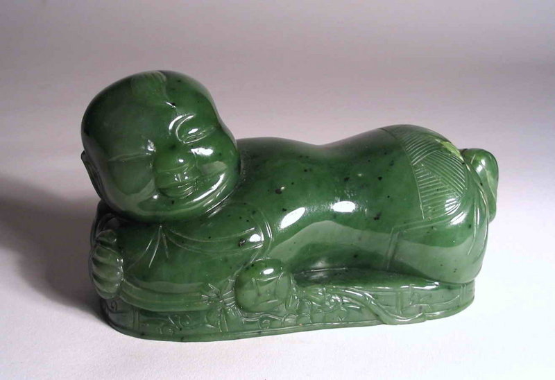 DESCRIPTION:  A wonderful Chinese carved nephrite figure of a reclining “lotus boy,” crafted from a beautiful medium-green jade with light and dark inclusions.  Here the smiling boy is depicted with head held up, feet tucked in, reclining on a lotus leaf with a seed pod under his left elbow.  An area of lighter inclusions is incorporated into the design as a lotus tendril climbing up the boy’s backside.  In Chinese folklore, such figures represent the hope for many sons - “as many as the seeds in the lotus pod.”  From a fine and long held Florida collection, it is in very good condition and dates from the Qing Dynasty, probably early 19th C.  DIMENSIONS:  4 ¾” long (12 cm) x 2 ½” high (6.4 cm).<div id='rater_target771078'></div>
