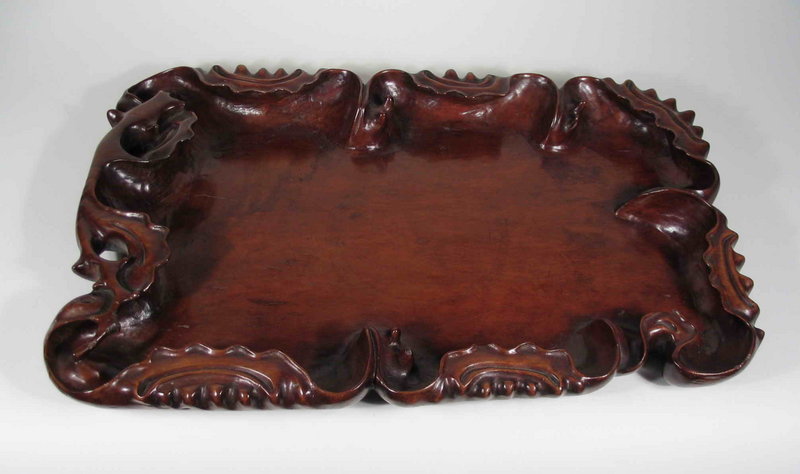 Sold and Shipped to Canada, Thanks<br /><br />
DESCRIPTION:  A very fine Chinese tea tray carved in high relief and crafted from beautifully figured longyan wood.  Skillfully hand carved in an irregular organic form depicting a lotus leaf with deeply upturned rims, the stem has been placed at one end with the edges throughout suggesting lotus pods with seeds. This gorgeous, large tray dates from the Qing dynasty, 18th C. PROVENANCE: From the Estate of Cynthia Phipps, NY.  CONDITION:  One repair to the end of the stem and one 2” age fissure on one side (see photos).  DIMENSIONS:  17 ¾” long (45 cm) x 12” wide (30.5 cm) x 2” high (5 cm).
<p>ABOUT LONGYAN WOOD: Longyan wood (meaning “dragon’s eye” in Chinese) is distinguished by its distinctively lustrous, highly figured grain which can appear to be striped, rippled or wavy. This grain pattern is created by the wood’s unique interlocking molecular structure. Its beauty is not easily revealed as the timber is difficult to season without splitting. Furthermore, its structure of interlocking and curling grain provides a demanding challenge for the most highly skilled craftsman. When a smooth unblemished surface is finally achieved, the finely textured timber reveals a rich golden tone and shimmering wave-like patterns that rivals the finest hardwoods. Its color can range from a dark reddish brown to light yellowish brown. Items made from longyan are becoming very scarce, and at the same time, newly appreciated by Chinese furniture collectors. Virtually all longyan furniture originates from Fujian province where it has been cultivated for centuries for its fruit. See “Arts of Asia,” Volume 34, Number 5 (September-October 2004) for an excellent article related to longyan furniture, with a photo of a very similar tray.
<div id='rater_target918159'></div>
