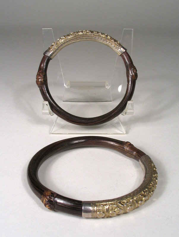 Pair - On Hold<br /><br />
DESCRIPTION: This matched pair of bracelets, truly wonderful examples of antique Chinese tribal jewelry, are crafted from dark brown bamboo branches bent in circular form with beautiful handcrafted bands of gold-washed silver. The repousse’ designs on the silver bands are composed of a pebble-like textured ground containing raised circular disks of coins or other good luck symbols.  Dating from C. 1900 and in excellent condition, these are beautiful tribal ornaments that are very wearable!  From a Florida collection. DIMENSIONS:  2 1/2” interior diameter (6.4 cm), 3 1/8” exterior diameter (8 cm).  
<div id='rater_target983179'></div>
