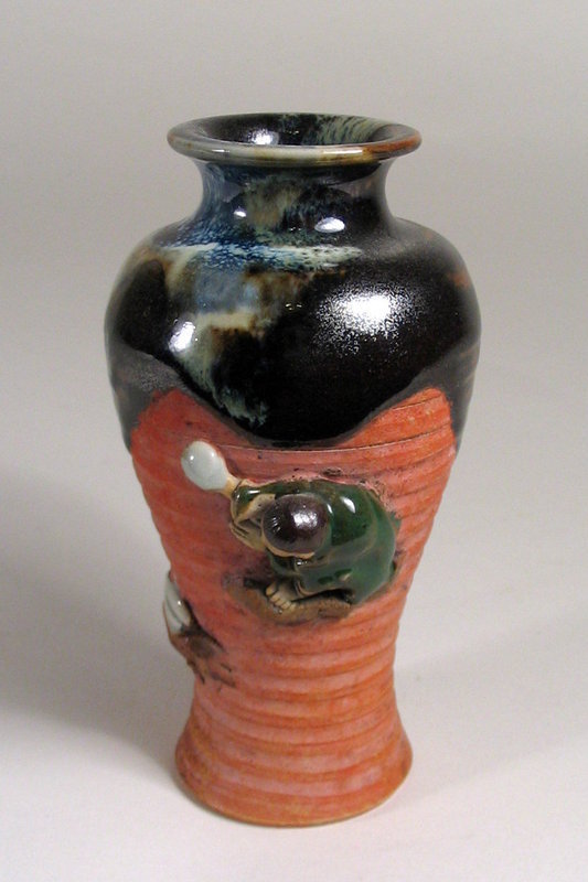 DESCRIPTION:  A small Japanese Sumida vase with round neck rim covered in a rich, thick flambe glaze running to the shoulders; a high relief figure of a young boy in a green robe is balanced upon rockery on the ribbed red body of the vase.  Excellent condition with no chips; unmarked base. DIMENSIONS:  4 3/4" high (12 cm) x 2 1/2" diameter (6.5 cm).  

<P>ABOUT SUMIDA EARTHENWARE POTTERY: This charming and highly collectable studio pottery originates from the Sumida River area in Japan (near Tokyo).  Produced primarily for export from the late 19th Century through the early 20th Century, this form of pottery is valued for the uniqueness of its handmade relief figures of people and animals engaged in various activities, often humorous or depicting scenes from folklore.  The tops are usually covered with a thick glaze in earth tones while the bodies of the pieces have an applied “cold paint” (usually red).
<div id='rater_target1197806'></div>
