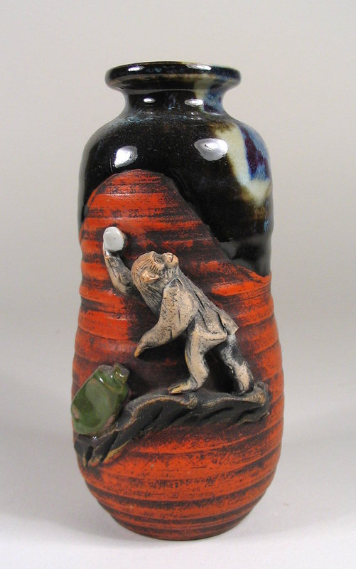 DESCRIPTION:  A Japanese Sumida vase with round neck covered in a rich, thick flambé glaze running to the shoulders, with a high relief figure of a monkey balanced on a rocky ledge.  In his right hand the monkey holds a peach (symbol of longevity) he has pulled from a green vase; these are all contrasted against the ribbed red body of the vase.  Excellent condition with no chips; signed "Ryosai" on the base. DIMENSIONS:  5 3/4" high (14.5 cm) x 2 1/2" diameter (6.5 cm).

<P>ABOUT SUMIDA EARTHENWARE POTTERY: This charming and highly collectable studio pottery originates from the Sumida River area in Japan (near Tokyo).  Produced primarily for export from the late 19th Century through the early 20th Century, this form of pottery is valued for the uniqueness of its handmade relief figures of people and animals engaged in various activities, often humorous or depicting scenes from folklore.  The tops are usually covered with a thick glaze in earth tones while the bodies of the pieces have an applied “cold paint” (usually red).
<div id='rater_target1207878'></div>

