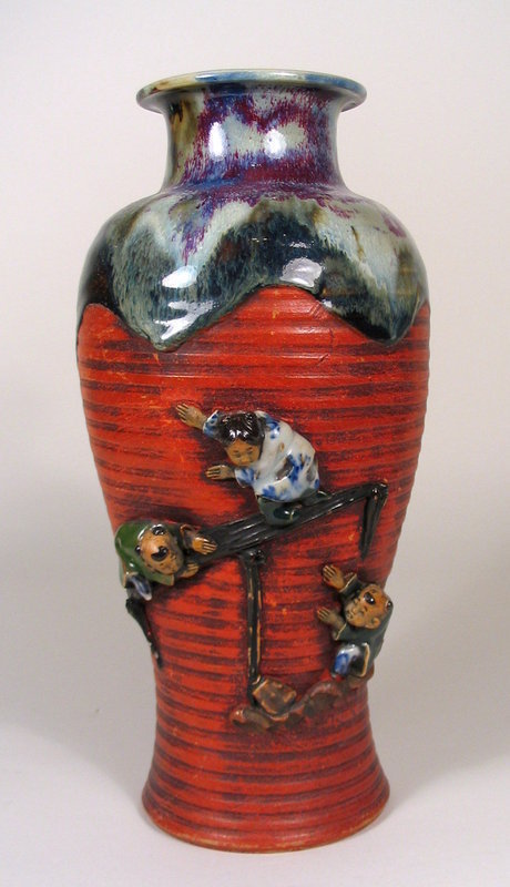 DESCRIPTION:  A large Japanese Sumida vase with three children in high relief playing on a bridge against the red ribbed body.  The neck rim is covered in a rich, thick flambé glaze that runs down the shoulders onto the traditional, cold painted body.  This vase is in excellent condition with no chips and very little rubbing.  DIMENSIONS:  11 1/2' high (29.2 cm) x 4 3/4" diameter (12 cm).

<P>ABOUT SUMIDA EARTHENWARE POTTERY: This charming and highly collectable studio pottery originates from the Sumida River area in Japan (near Tokyo).  Produced primarily for export from the late 19th Century through the early 20th Century, this form of pottery is valued for the uniqueness of its handmade relief figures of people and animals engaged in various activities, often humorous or depicting scenes from folklore.  The tops are usually covered with a thick glaze in earth tones while the bodies of the pieces have an applied “cold paint” (usually red).
<div id='rater_target1221264'></div>
