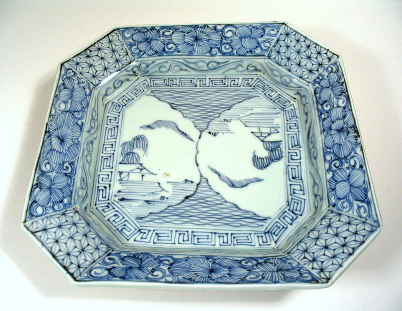 DESCRIPTION:  A Chinese eight-sided footed plate with raised base and blue under-glazed decorations featuring two pavilions by the water (each reversed so the plate can be viewed upright from two directions), surrounded by key-fret and floral borders.  Collector's stickers on back indicate the number of the piece and the date the USA collector originally purchased it (April 14 of 1977).  Excellent condition with no chips, cracks or repairs; small original firing flaws. DIMENSIONS:   9 7/8" square (25 cm);  stands 2 7/8" high (7.3 cm).<div id='rater_target1237238'></div>
