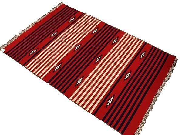 DESCRIPTION:  A large, vibrant Churro wool blanket from the weaving center of Chimayo in Northern New Mexico.  This finely woven blanket is of the "Rio Grande" style with alternating bands of white and navy stripes running across a bright red ground.   These bands are each separated by a line of three stars with twelve points.  CONDITION:  This reversible blanket is in excellent condition with no repairs, holes or stains; the fibers are thick and the colors vibrant.  
<p>CULTURAL BACKGROUND:  The patterns on Chimayo textiles are creative masterpieces of design and color, and have a rich cultural history.  Spanish immigrant families of Northern New Mexico first began weaving in the village of Chimayo in the early 17th C. (1610-20), bringing a distinct Spanish weaving tradition with them.  They also brought their favorite breed of sheep to New Mexico, the Navajo-Churro or Churro.  This sheep is renowned for its hardiness to extremes of climate, and is favored for its non-oily, two layer wool coat.  For hundreds of years these families used wooden floor looms and the wool of the Churro sheep to create blankets, rugs and textiles to keep them warm during the cold New Mexico winters. This tradition continues today.  Within the small Northern New Mexico village of Chimayo,  Navajo people and descendents from the original families continue to weave beautiful textiles. 
<p> DIMENSIONS:  84" long (not including fringe) x 52 1/2" wide. 
<div id='rater_target1268453'></div>

