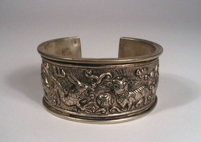 DESCRIPTION: A charming and well executed Chinese silver tribal bracelet, the wide band framed with parallel lines between which various mythical and humorous animals cavort. Included in the hand crafted repousse processional are donkeys, fish, and a dragon vying with a foo dog for a brocade ball. This tribal bracelet comes to us from one of the mountainous Miao groups, who are well known for their beautiful silver work.  Estimated to date from the first half of the 20th century and in very good condition.  DIMENSIONS:  An outside diameter of 3 1/8” (8 cm); band is 1 ½” wide (3.8 cm).  <div id='rater_target1279168'></div>
