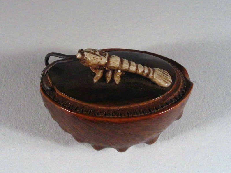 DESCRIPTION: An unusual netsuke featuring an abalone shell crafted from wavy burl wood with an ivory lobster perched on top.  The lobster’s curled antennas are made of metal, and on the underside of the shell a signature is etched into the wood.  Early to mid 20th century in very good condition.  DIMENSIONS: 1 ¾” long (4.5 cm).  <div id='rater_target1283858'></div>

