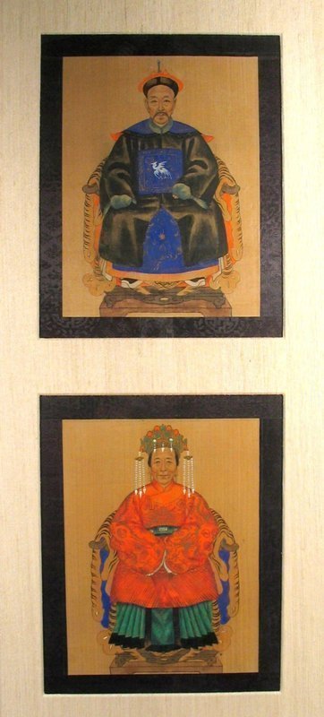 DESCRIPTION:  A pair of rare Qing Dynasty (early 1800's) ancestor portraits of miniature size, framed in an archival, off-white silk matt. Both figures are seated on horseshoe back chairs with tiger skin drapes, the husband in a bright blue robe with black silk overcoat, his rank badge displayed on his chest; the wife in a bright orange-red coat, teal colored skirt, and elaborate headdress.  Both are well painted with detailed, lifelike features.  Portraits of this size are very rare as most ancestor portraits are quite large. These are in excellent condition and would add a beautiful accent to a home displaying Chinese art or antiques.  DIMENSIONS:   Actual portrait sizes:  9" high (22.9 cm) x 6 7/8" wide 17.5 cm) each.  Frame dimensions:  33 1/4" high (84.5 cm) x 15 3/4" wide (40 cm).  
<p>CULTURAL BACKGROUND: The Chinese have long had a profound connection to their ancestors. They believe that death does not sever a person’s relationship with the living and that, if properly worshipped and honored in private family rituals, the spirits of their ancestors can bring them health, long life, prosperity and children.  In Imperial China, filial sons of all classes, as part of their sacred duty to care for the spirits of their ancestors, paid homage to them in ritual ceremonies.  Chinese commemorative portraits, commonly referred to as "ancestor paintings," were painted specifically for use in ancestor worship. Besides being compelling art, the paintings reveal much about Chinese social and cultural history.  With the development of photography in the 19th century, the painting of ancestor portraits began to wane. 


<div id='rater_target1285146'></div>
