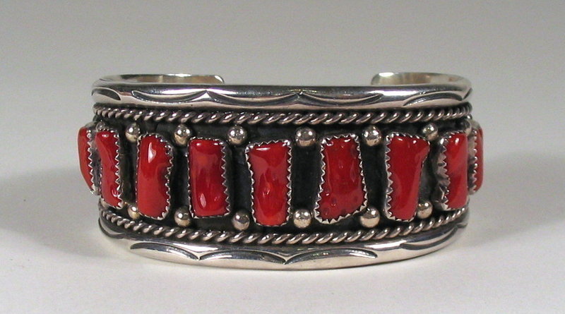 DESCRIPTION:  A beautifully crafted Navajo sterling and natural coral cuff bracelet .  This bracelet features thirteen natural, dark red coral stones mounted on a 1 1/8" wide silver cuff between a scrolling border of stamp work, twisted wire, and silver beads.  This cuff looks beautiful on the wrist; the inside is stamped "STERLING."  See the last photo showing this bracelet with other pieces from our Native American jewelry collection. DIMENSIONS:  6 1/2" circumference (16.5 cm);  medium adult size.  The circumference is the total measurement around the inside, including the gap between the ends, which is also the approximate wrist size.  Weight is 2.15 oz. (60 grams).  Please see the last photo where the size is compared to our recently listed Bisbee turquoise cuff (stock #W-JO10). <div id='rater_target1289162'></div>
