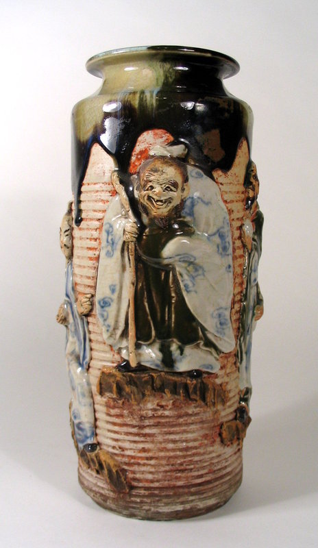 DESCRIPTION:  A large and quite fantastic Sumida Gawa vase with ribbed body, four large figures in high relief, and wide flared mouth.  A thick, traditional flambe' glaze in dark brown and white covers the mouth and neck, and flows down the shoulders.  Fine attention to detail has been paid to the four large handmade figures, all characters from Japanese lore, standing on ledges against the ribbed body.  Inoue (Ryosai) maker's mark in oval-shaped appliqué toward the base, representing a family of three generations of potters who made Sumida wares at the family kiln in Yokohama.  Early 20th C. and in perfect condition; no chips or repairs.  See final photo for size comparison with some of our other Sumida listings.  DIMENSIONS:   12 1/2" high (31.7 cm) x 6" diameter (15.3 cm).  

<P>ABOUT SUMIDA EARTHENWARE POTTERY: This charming and highly collectable studio pottery originates from the Sumida River area in Japan (near Tokyo).  Produced primarily for export from the late 19th Century through the early 20th Century, this form of pottery is valued for the uniqueness of its handmade relief figures that include people and animals engaged in various activities, often humorous or depicting scenes from folklore.  The tops are usually covered with a thick glaze in earth tones while the bodies of the pieces have an applied “cold paint” (usually red or black).  
<div id='rater_target1291308'></div>
