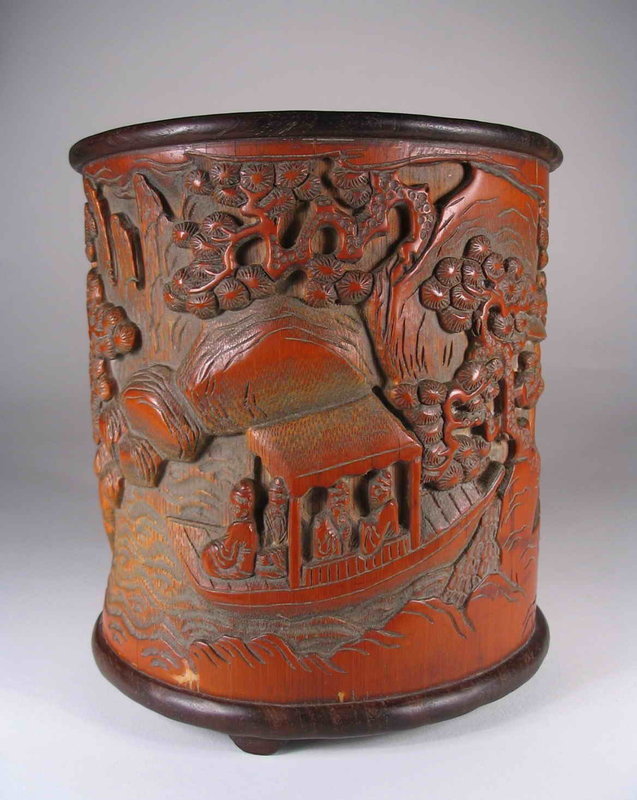 DESCRIPTION: A good Chinese scholar’s brushpot, carved in deep relief with a continuous mountain landscape scene framed by gnarled pine trees and depicting two groups of scholars, some examining a scroll and others in a boat.  The base and rim are encased in hardwood and the pot is engraved with a two line inscription. Very good condition, latter Qing Dynasty, 19th to early 20th C.  DIMENSIONS:  6 ½” high (16.5 cm) x 6” diameter (15.2 cm).<div id='rater_target1291632'></div>
