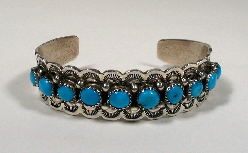 DESCRIPTION: A stunning Navajo sterling silver Bisbee blue turquoise cuff bracelet by Navajo silver artist, Henry Davis.  Ten heavenly blue cabochons are set between silver beads and scalloped silver edges which are stamped in a sunburst design. This is a truly beautiful bracelet, very wearable, and in perfect condition with no chipped stones.  The inside is hallmarked "HD" and stamped "Sterling."  If you desire a bracelet with matching necklace, see the last two photos where this bracelet is shown with our necklace #W-JO12.  Although crafted by different artists, they are a beautiful marriage with similar sized stones and the same beautiful Bisbee blue color. DIMENSIONS:  Weight is 1.25 oz. (35g); wrist size is 6 3/8" including opening (size is adult, medium).  <div id='rater_target1292011'></div>
