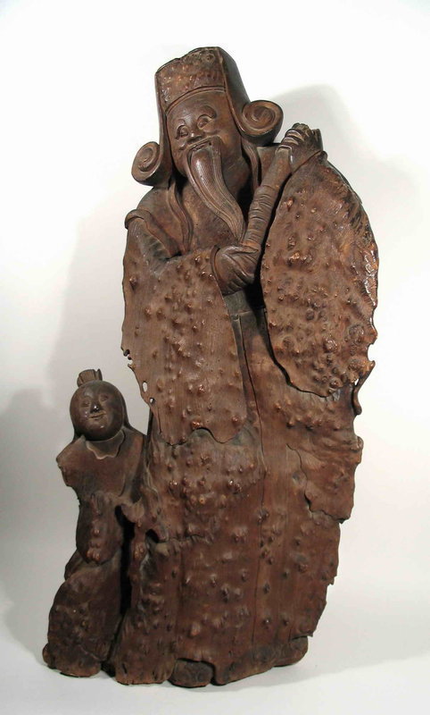 DESCRIPTION:  A significant Chinese sculpture featuring a Scholar with his boy attendant, carved from a large slab of burl hardwood.  The undulations and knobs of the slightly curving burl slab have been beautifully incorporated into the carving, forming the scholar’s garment and top of his curled hat. The bearded scholar looks slightly upward with a pleasing expression and holds a scroll in his hands.  At his side is his young attendant gazing upward with a charming smile. Naturalistic burl carvings have a long and esteemed history in China, but rarely does one find such a genuinely old carving of this size.  From the estate of heiress Cynthia Phipps of New York, NY, and dating from the Qing Dynasty, 18th C.  CONDITION:  Small worm holes scattered throughout, stable split in beard, tip of scroll has old break.  DIMENSIONS:  40” high (1.02 m) x 19” wide (48.3 cm). <div id='rater_target1299472'></div>
