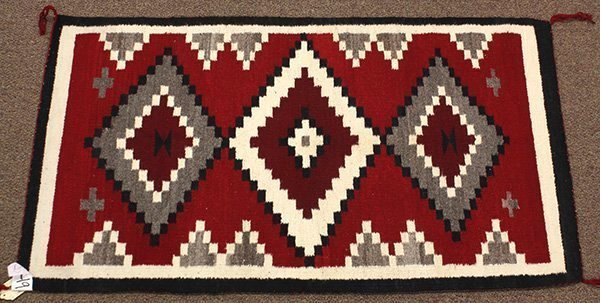 DESCRIPTION:   A small Navajo rug made of handspun wool in an "Eye Dazzler" pattern of three vibrant, serrated diamonds on a bright red ground, enclosed with a double border of white and black.  The Eye Dazzler, so named by early traders because of the intense coloring of the dyes, is a serrated design that was woven in multiple colors of bright aniline dyed yarns in the 1880 - 1890 period.  Navajo Eye Dazzler weavings were influenced by the Mexican satillo weavings and the Germantown yarn weavings.  This rug dates to the mid 1900's and is in very good condition with no stains, fading or losses.  DIMENSIONS:  47 1/2" long (slightly over 1.2 m) x 27" wide (68.5 cm).  

<div id='rater_target1301287'></div>
