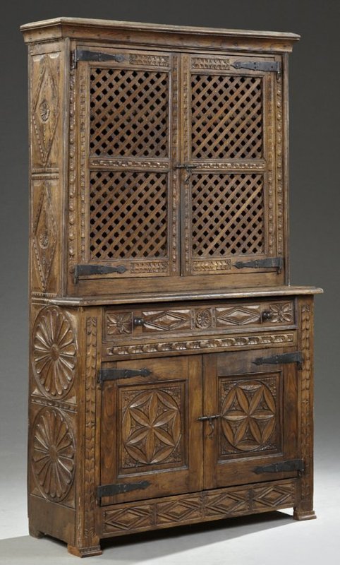 DESCRIPTION:  A Spanish carved oak buffet a deux corps (buffet or hutch with the top cabinet having a shallower depth than the bottom), 19th C.  The carved cavetto molding crowns double lattice work cupboard doors with hand forged iron hinges which open to reveal two interior shelves.  These are set on a base with a frieze drawer over double cupboard doors, also with iron hinges, each carved with a six point flower set within a circle.  Flanking the doors are beautifully carved sunburst side panels, with the whole resting on square feet joined by a diamond carved skirt. CONDITION: This is a sturdy piece. Some mild chip and scuff wear are noted intermittently, consistent with age and use.  A superb example from a New Orleans estate.  DIMENSIONS:  78.25" high (almost 2 meters) x  46.25" wide (1.17 m) x 17.25" deep (43.8 cm).  <div id='rater_target1302577'></div>
