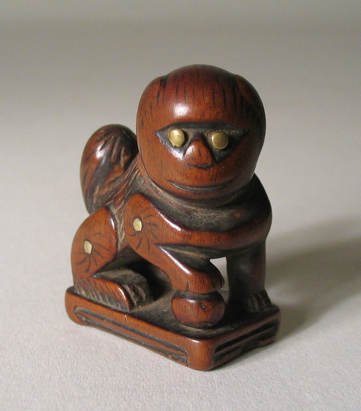 DESCRIPTION: An appealing Chinese toggle (guajian), carved from Huanghuali wood (a hardwood similar to Rosewood) in the form of a Buddhist lion seated on a plinth with one paw placed on top of a ball.  With raised tail, textured fur on his back, and brass studs decorating the eyes and each limb, this foo dog would have been used as a counterweight for a tobacco pouch or other object suspended from a belt.  Displaying a luscious patina from use and handling, this little grinning lion is a real charmer and a wonderful Chinese folk art piece; 18th C.  DIMENSIONS:  1 ¼” wide (3.2 cm) x 1 ½” high (3.8 cm).  <div id='rater_target1308231'></div>
