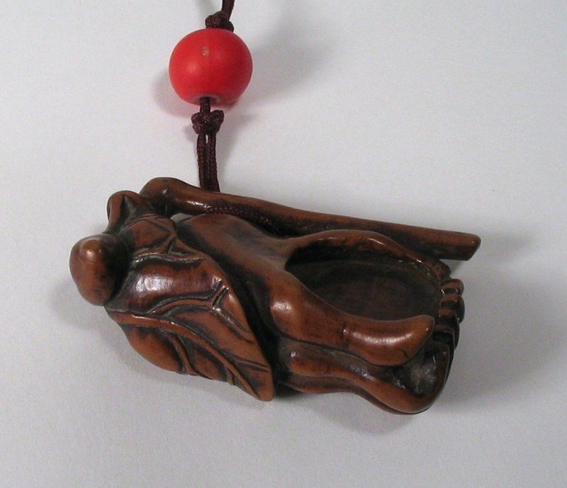 DESCRIPTION:  An antique Chinese toggle (guajian), carved from boxwood in the form of a Buddha's hand fruit (or fingered citron), a symbol of happiness, longevity and good fortune in China. The fingered citron is unusually shaped with bright yellow fruit segmented into finger-like sections, resembling a human hand.  Highly fragrant, it is used predominantly in China for perfuming rooms and personal items such as clothing.  According to Buddhist tradition, the Buddha prefers the "fingers" of the fruit to be in a closed position where they resemble hands in prayer.
 
<p>This toggle has a luscious, old boxwood patina that only comes from age and handling.  It's carver included multiple symbolisms in this little work of art: "closed fingers, open hand" (symbolizing prayer), capped with a sacred lotus leaf (eluding to Buddha's enlightenment vision), and topped with a lingzhi mushroom (symbolizing immortality).  The toggle is strung with a cord through the openings in the stem, and is tied in place with a coral bead.  It would have hung from a belt or sash, serving as a counterweight to a tobacco pouch or purse; a wonderful antique Chinese folk art piece, 18th C.  DIMENSIONS:  2" long (5.1 cm) x 1.25" wide (3.2 cm). 
<div id='rater_target1308901'></div>
